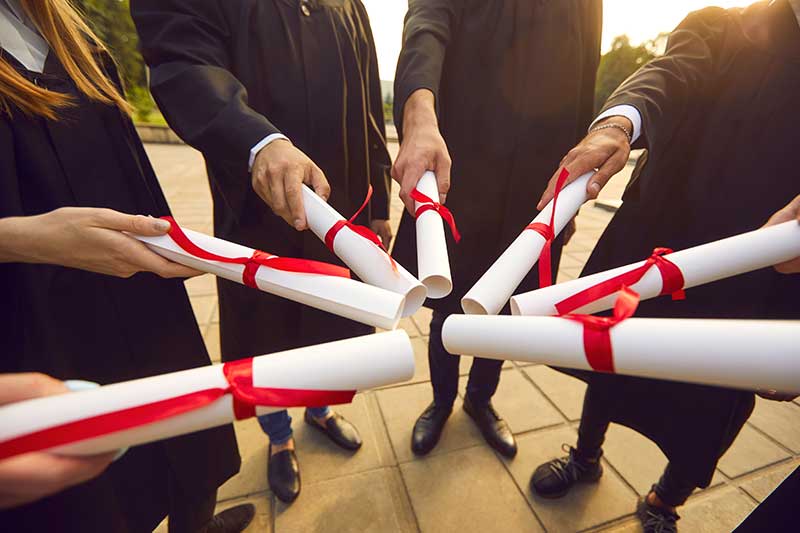 graduates in a circle holding their rolled up diplomas that are tied with red ribbons to touch each other. We'd love to have them at one of the best graduation party places in quincy ma - the fox & hound!